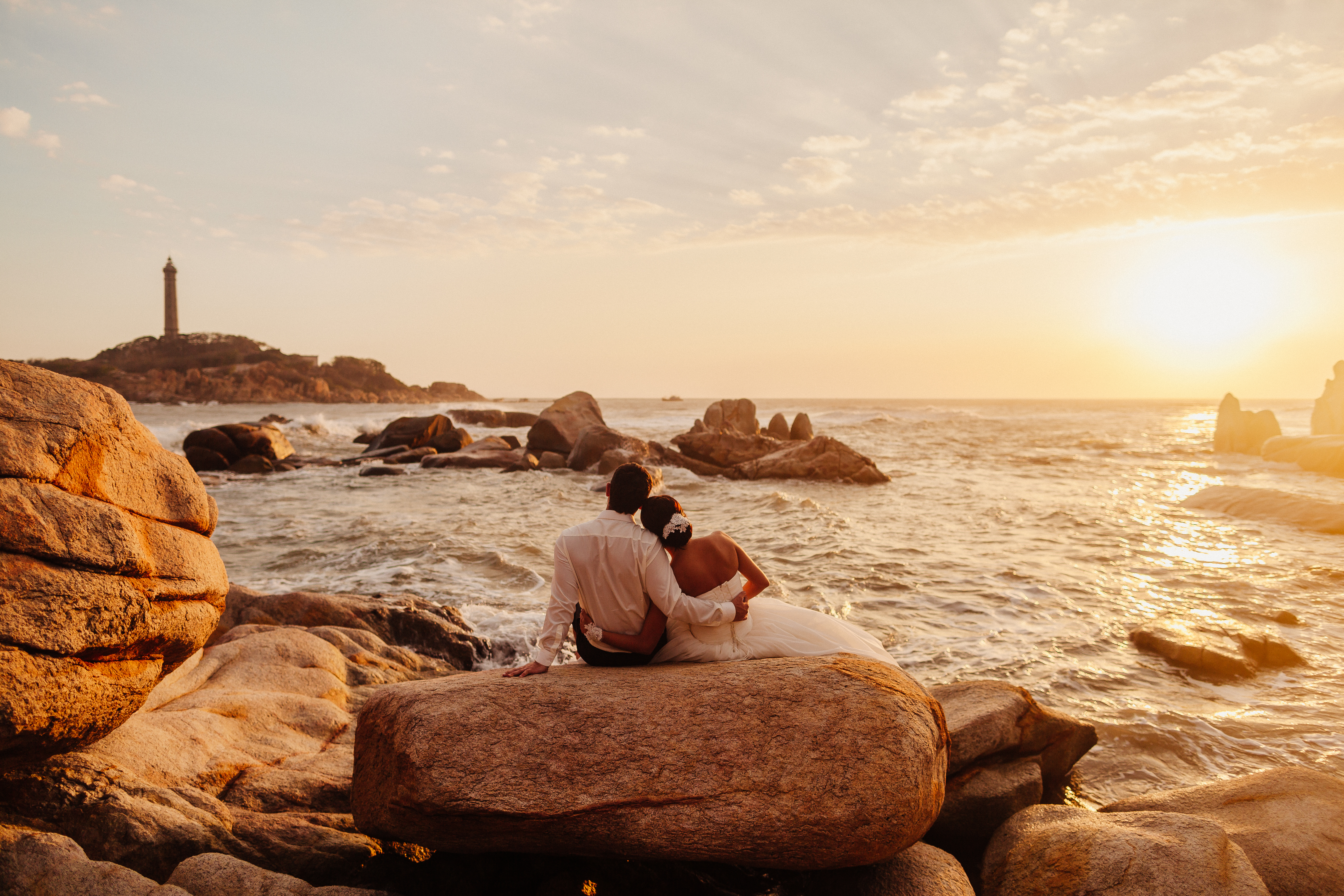 Couple sitting on rocks by the ocean at sunset